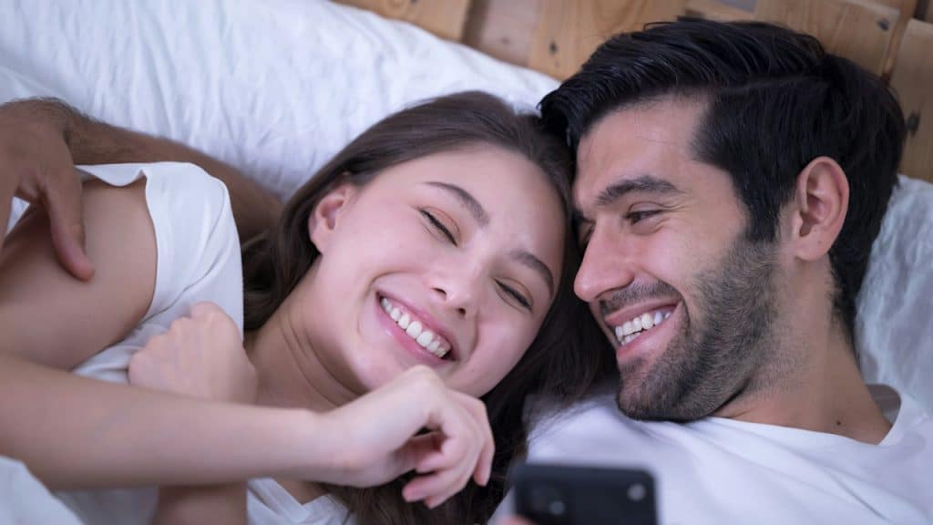 A young couple in a bed with mobile phones.