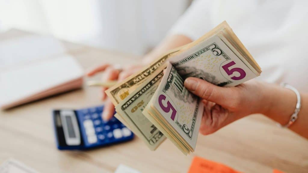 A hand counts cash beside a calculator.