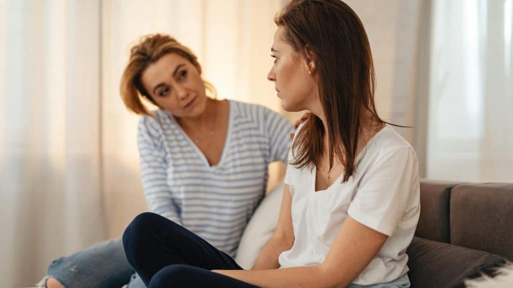 A woman comforting another woman sitting on a couch.