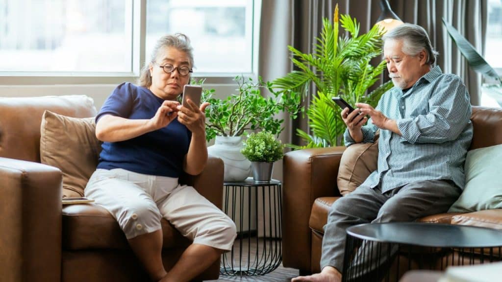 Elderly couple on leather chairs using their separate mobile phones in a living room.