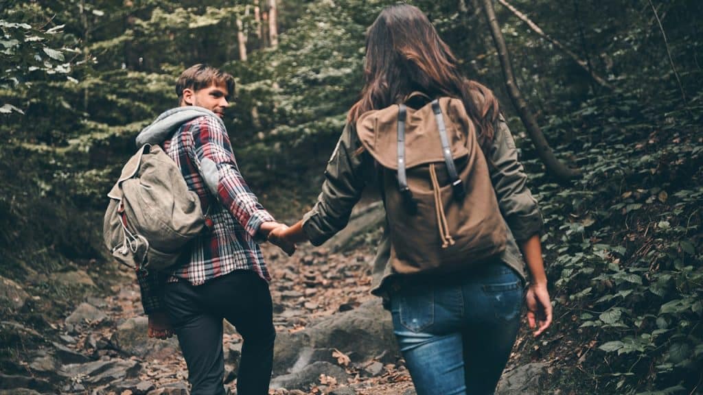 A couple hiking together, with the man supporting the woman by holding her hand as she climbs.