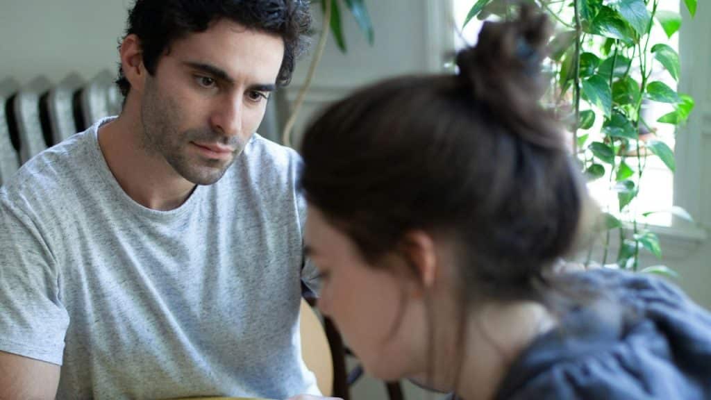 A man in a light grey t-shirt looks intently at a woman with dark hair.