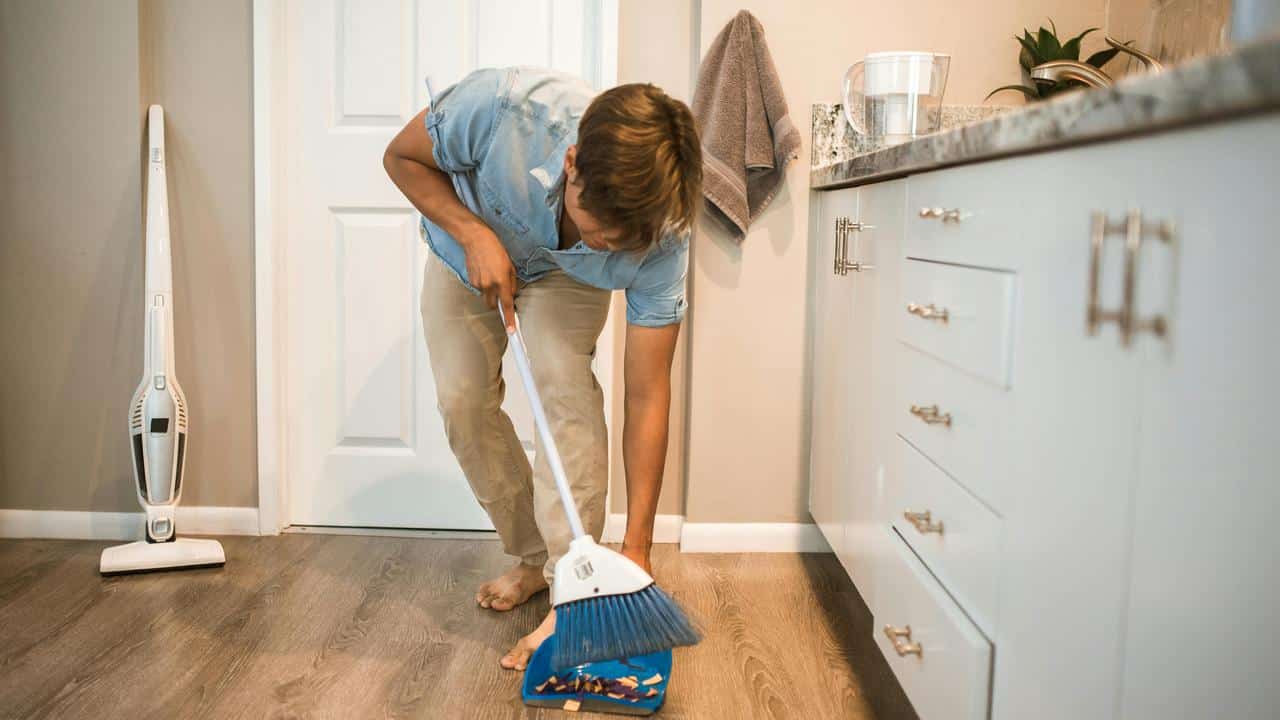 A man sweeping the kitchen floor into a dustpan.