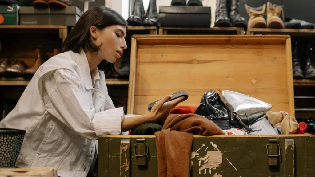 A woman looking through items in an open trunk while holding a smartphone.
