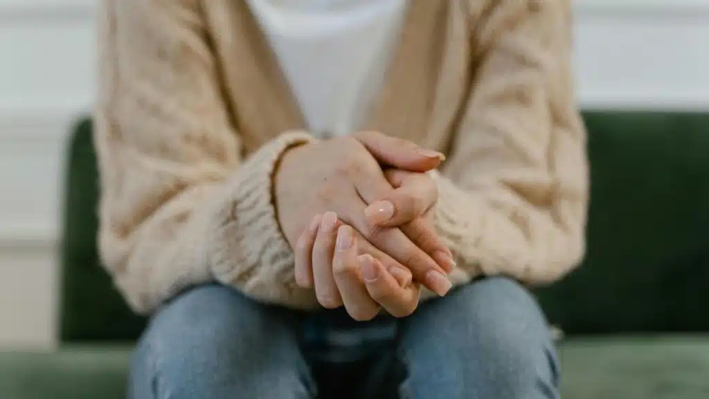 A person sitting with their hands clasped in their lap.