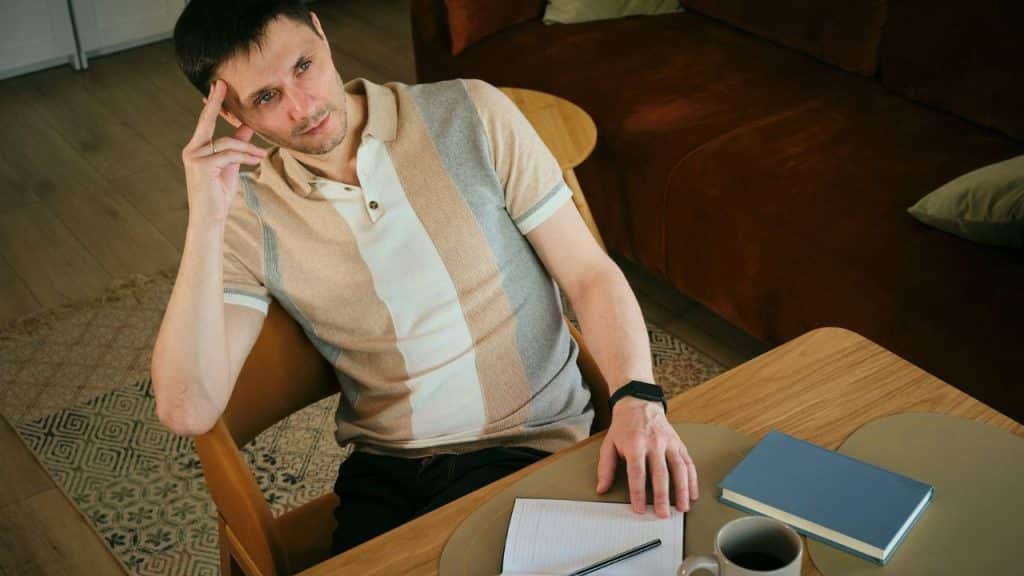 A man in a striped shirt sits at a table with a notebook and book.