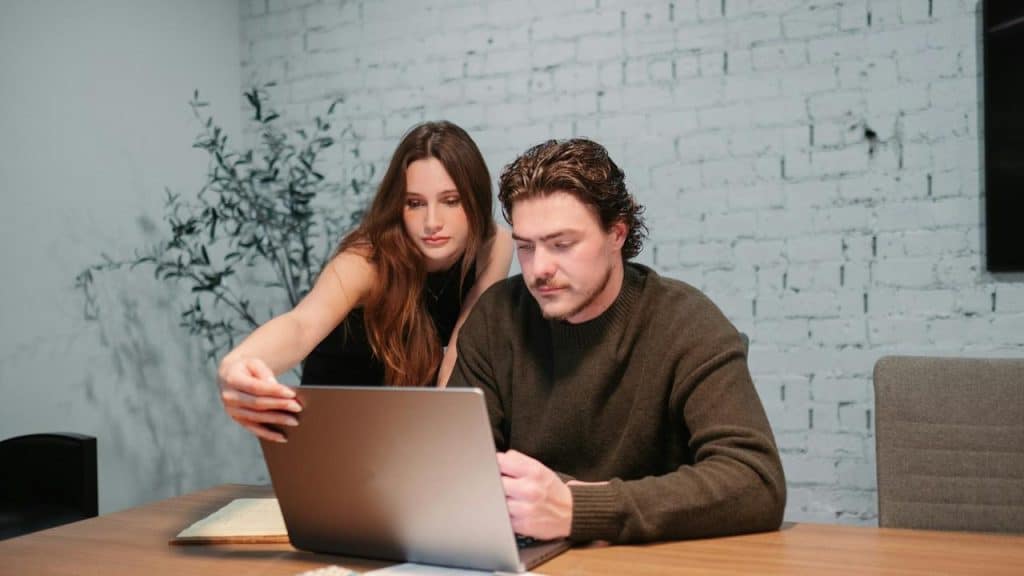 A man and woman sitting at a table looking at a laptop.