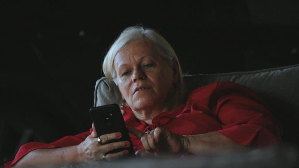 A woman in a red long-sleeve shirt holding a black smartphone.