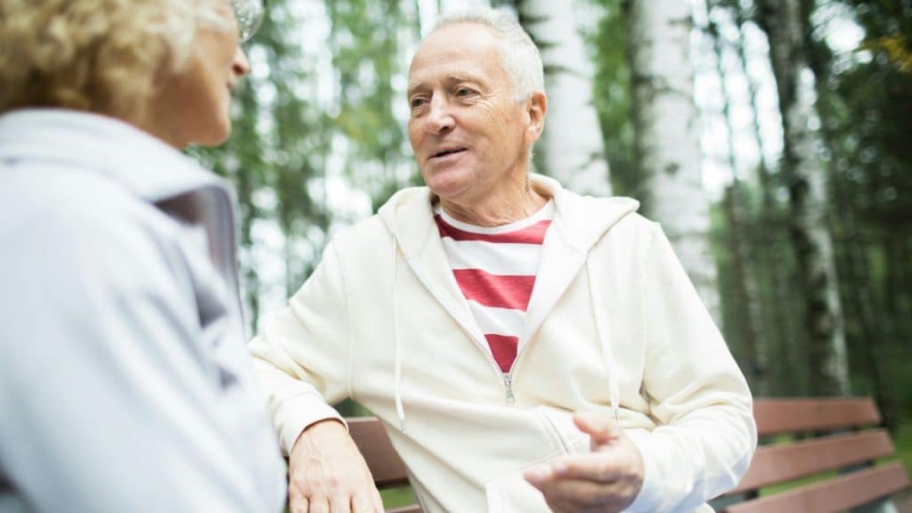 Older man in a white and red striped shirt talking to a person in a park.