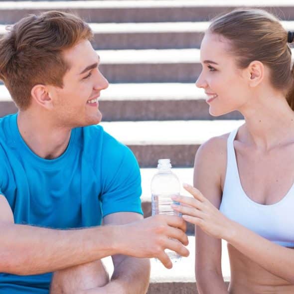 Side view of a beautiful young couple in sports clothing sitting on stairs face-to-face and smiling.