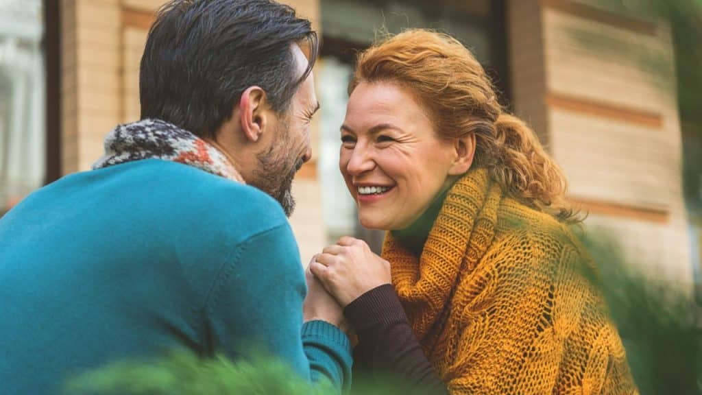 Happy middle-aged couple holding hands, smiling and looking into each other's eyes outside.