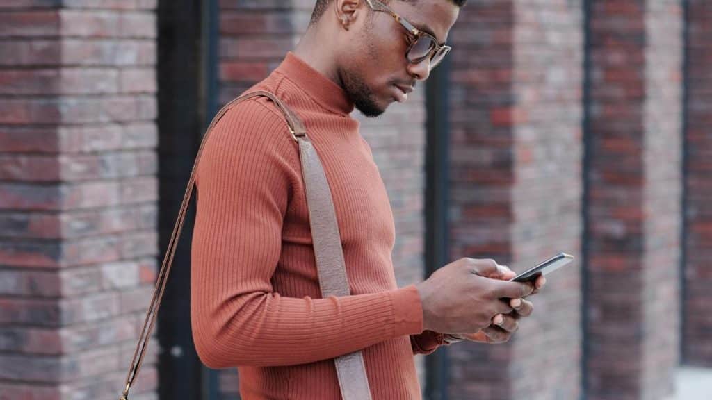 A man in a brown turtleneck using a smartphone outdoors