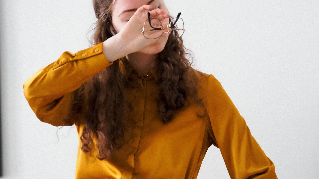 A woman in a yellow shirt holding a pair of glasses.