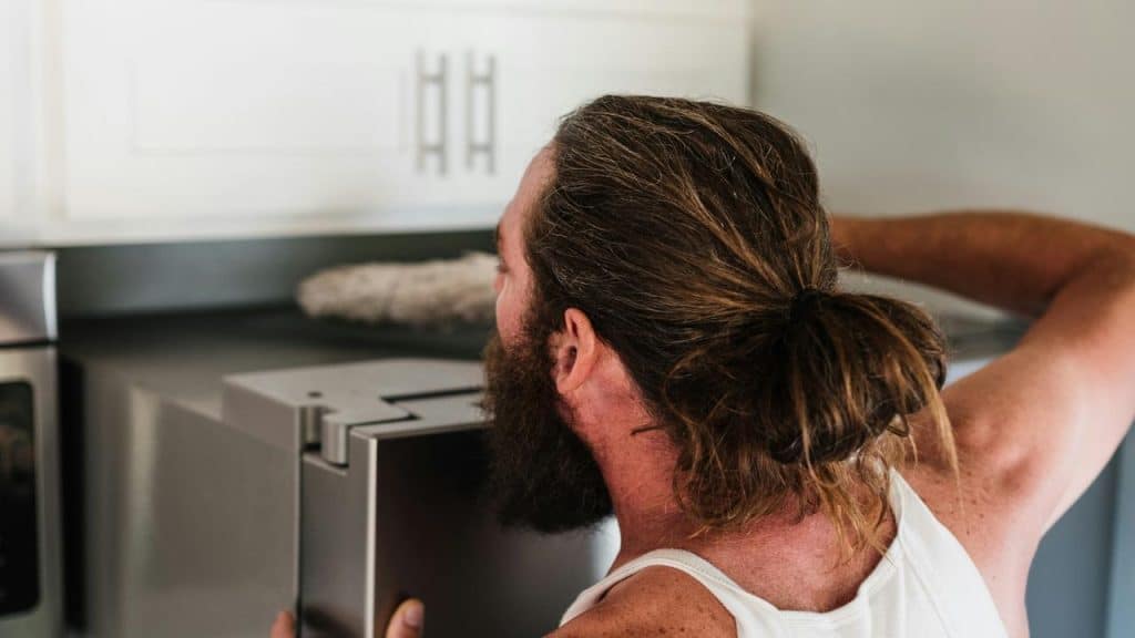 A man with a beard and ponytail looks into a refrigerator.