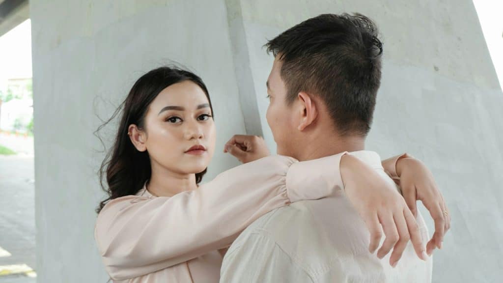 A woman leaning her arms on a man’s shoulder, standing next to her.