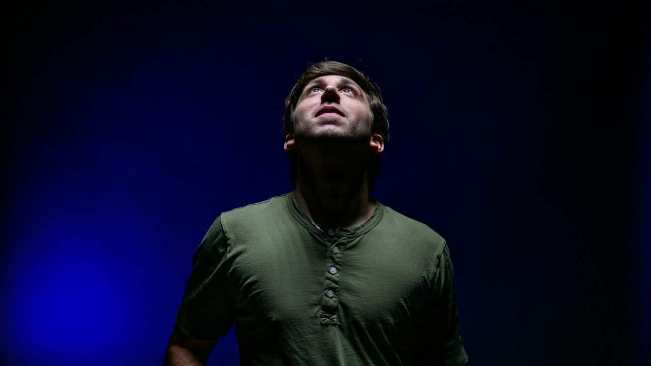 A man in an olive green shirt looking up against a dark blue background.