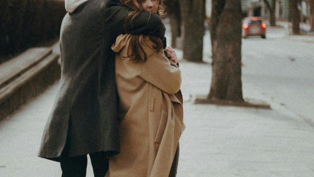 A couple hugging on a sidewalk in an urban street.
