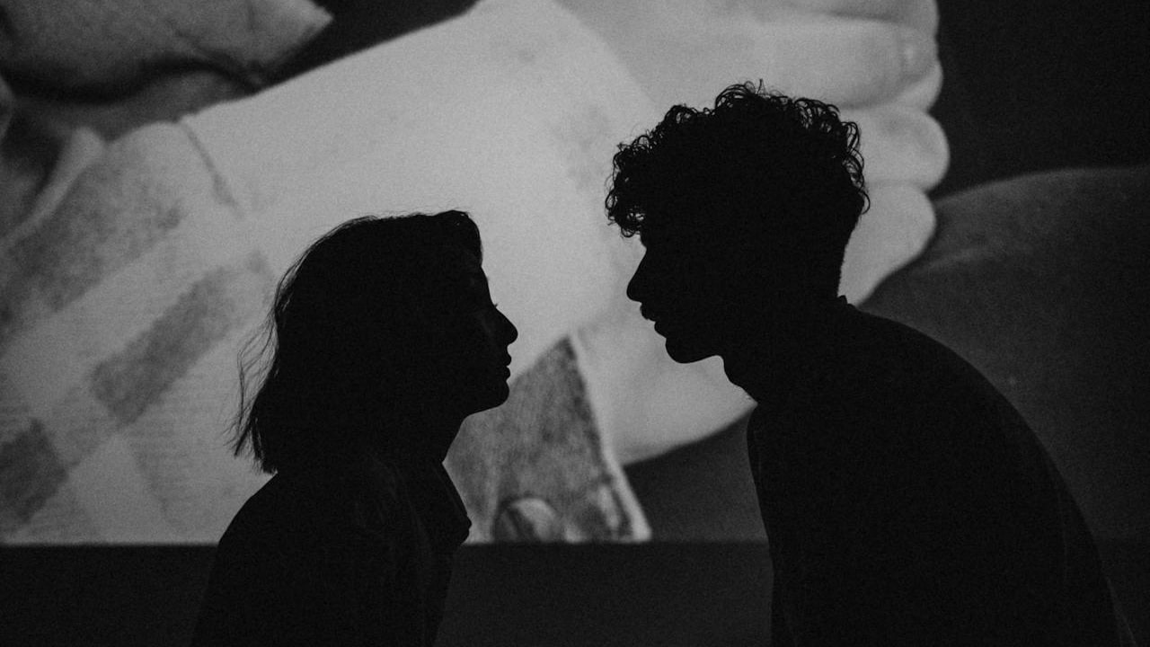 A black and white silhouette of a couple facing each other, with a projected image of hands clasping in the background.