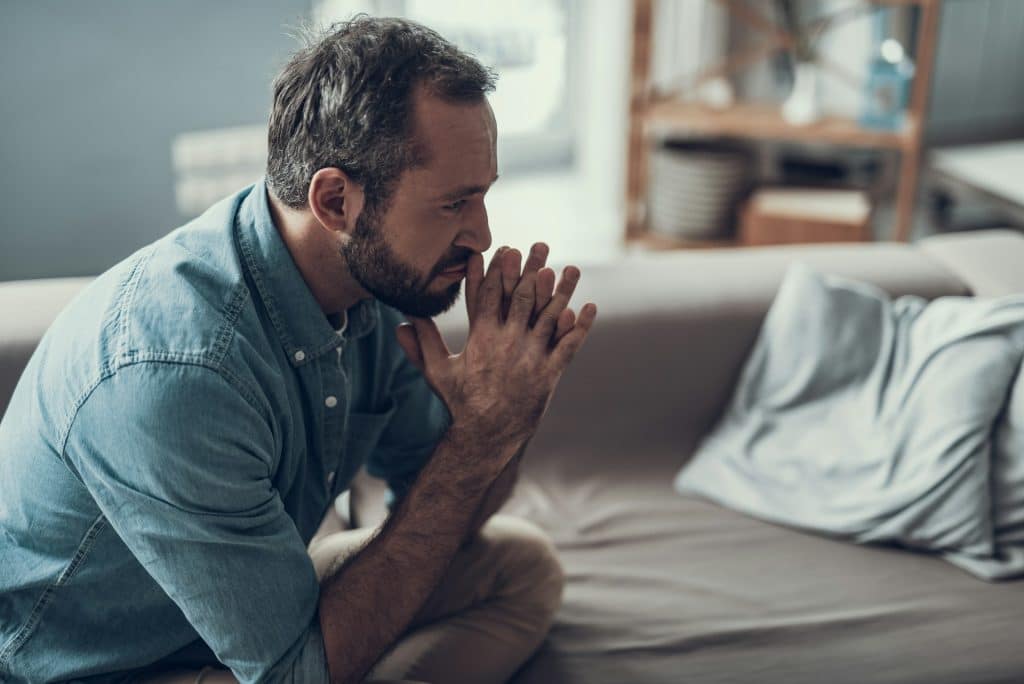 A man sitting on the couch while thoughtfully looking away.