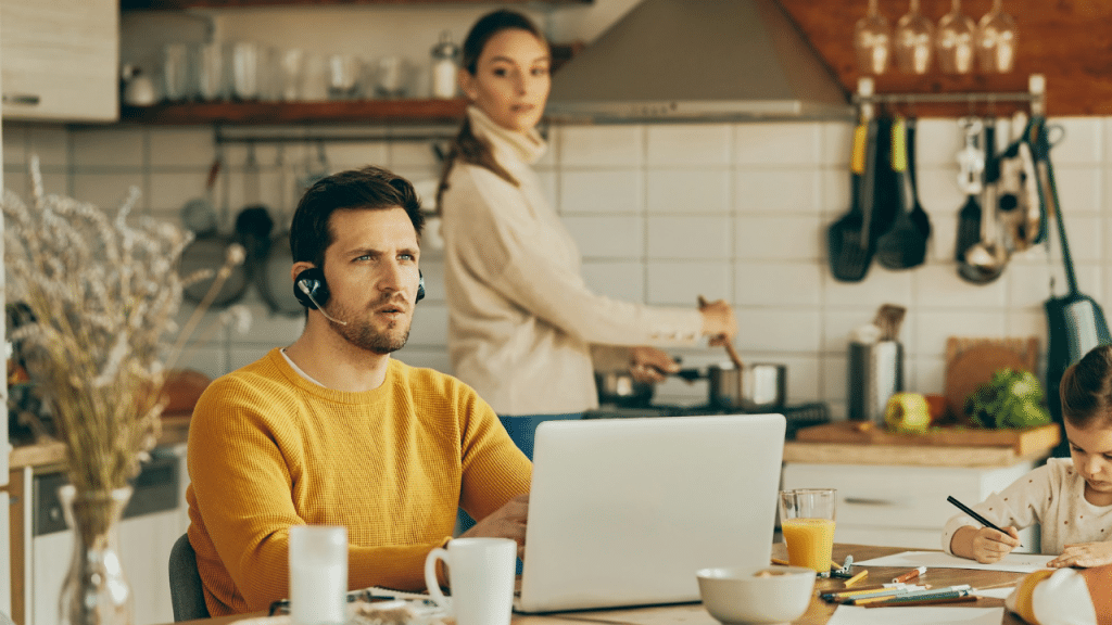 Man working on a laptop, woman cooking, and child drawing in a kitchen.