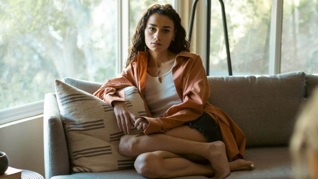 Woman sitting cross-legged on a couch looking directly at the camera indoors.