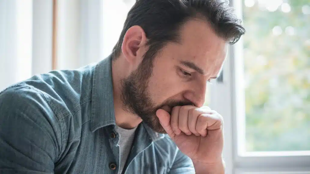 Close-up of a frustrated or pensive man holding his hand near his mouth.