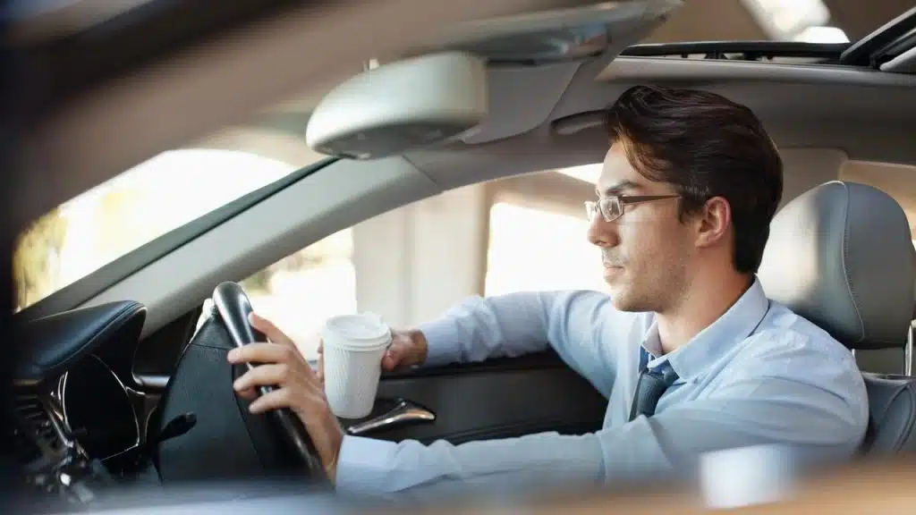 A man in a car holding a coffee cup while driving.