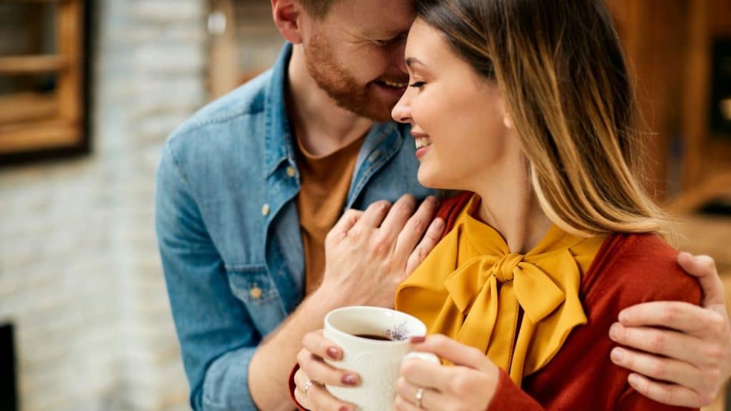 Close-up of a smiling couple embracing, the woman holding a white coffee mug.