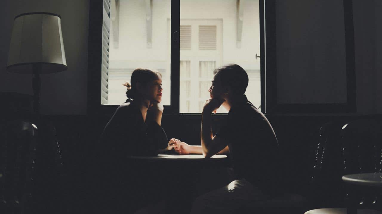 A couple holding hands at a table by a window.