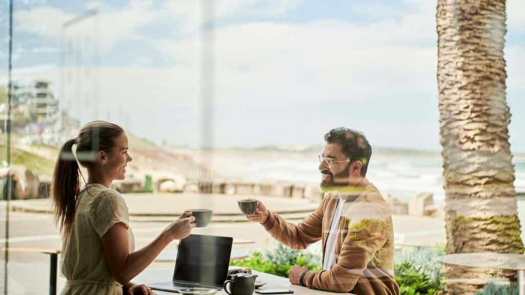 A man in a brown jacket sitting beside a woman at a coffee shop.