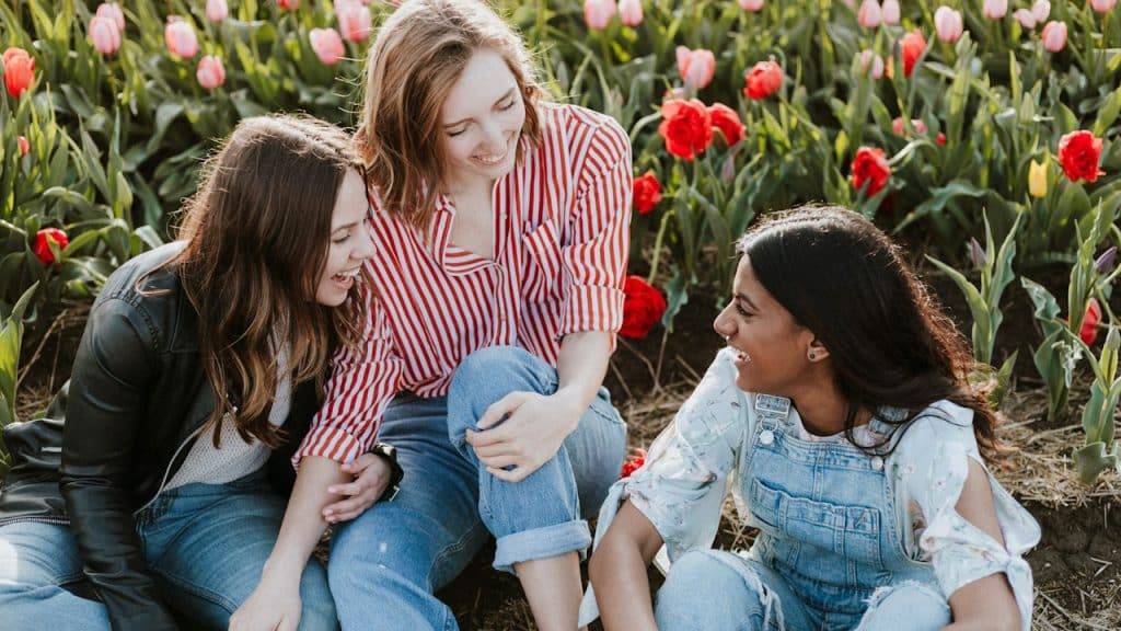 Three women sitting near flowers.
