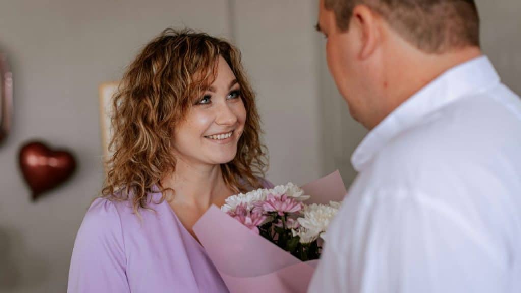 A smiling woman with curly hair holds a bouquet of flowers given by a man.