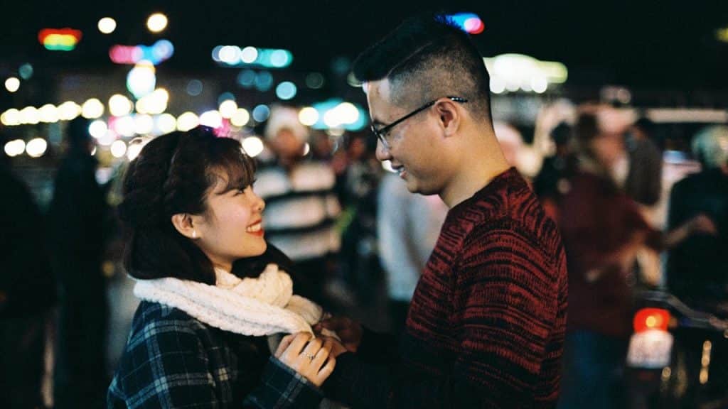 A happy couple smiling at each other on a crowded, brightly lit street at night.
