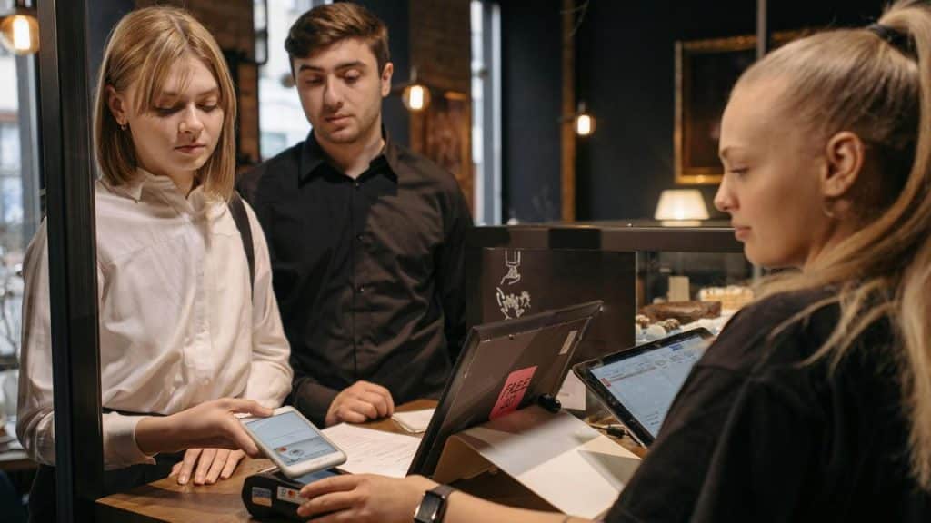 A woman using her phone to pay at a café counter while a man stands beside her.