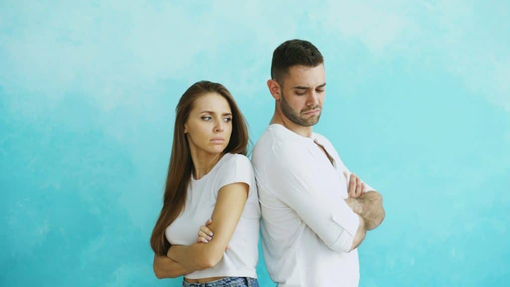A couple standing with their backs to each other and looking upset with each other.