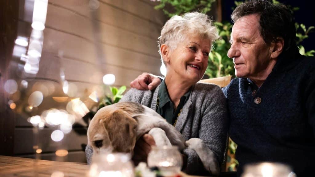 Elderly couple sits outside at night, holding a beagle dog and smiling at each other.