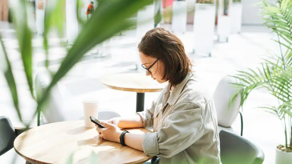 A person sitting at a cafe table using a smartphone.