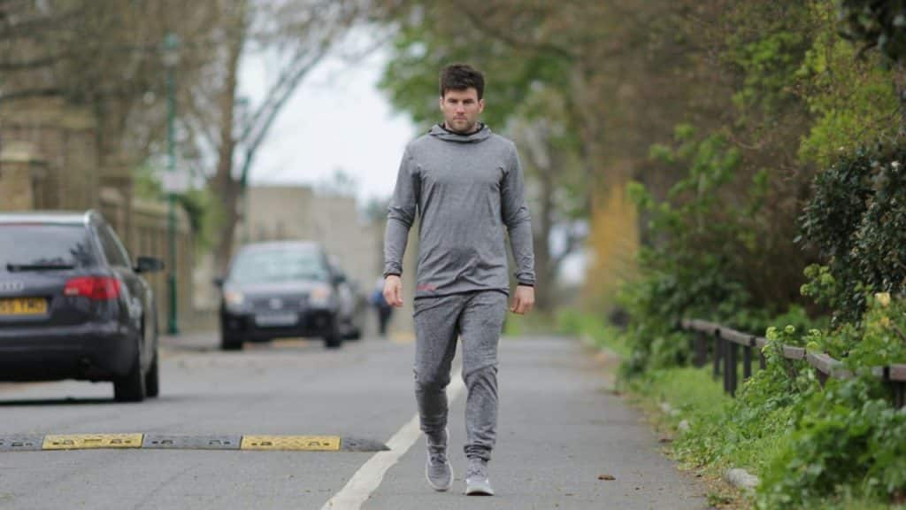 Man in grey athletic wear walking on a paved path next to a road.