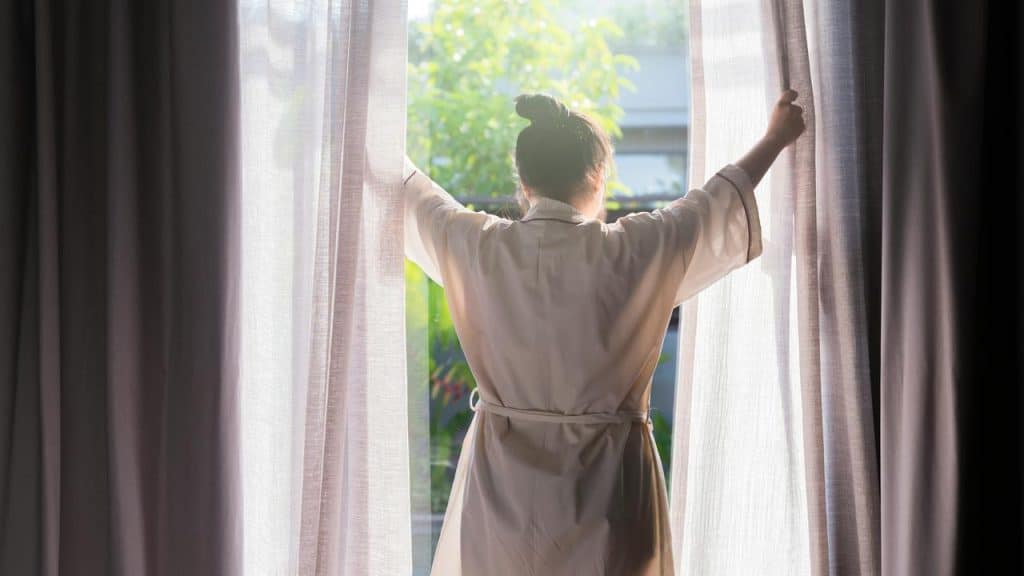 A person opening curtains to let in morning light.