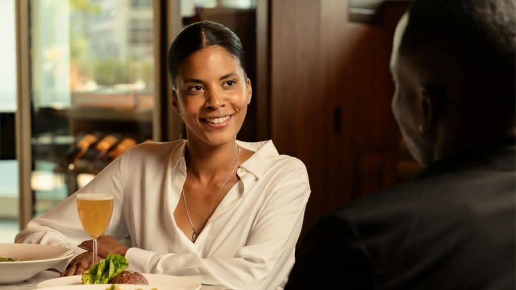 Woman in white shirt smiling at person across a restaurant table with a drink.