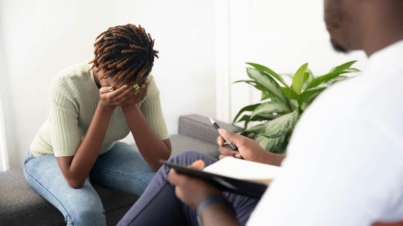 A distressed woman sitting with her head in her hands while talking to a therapist.