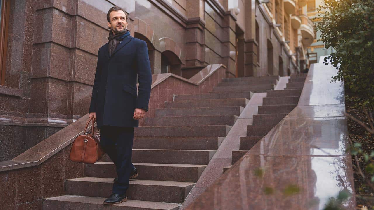 A man walking down outdoor steps holding a leather bag.