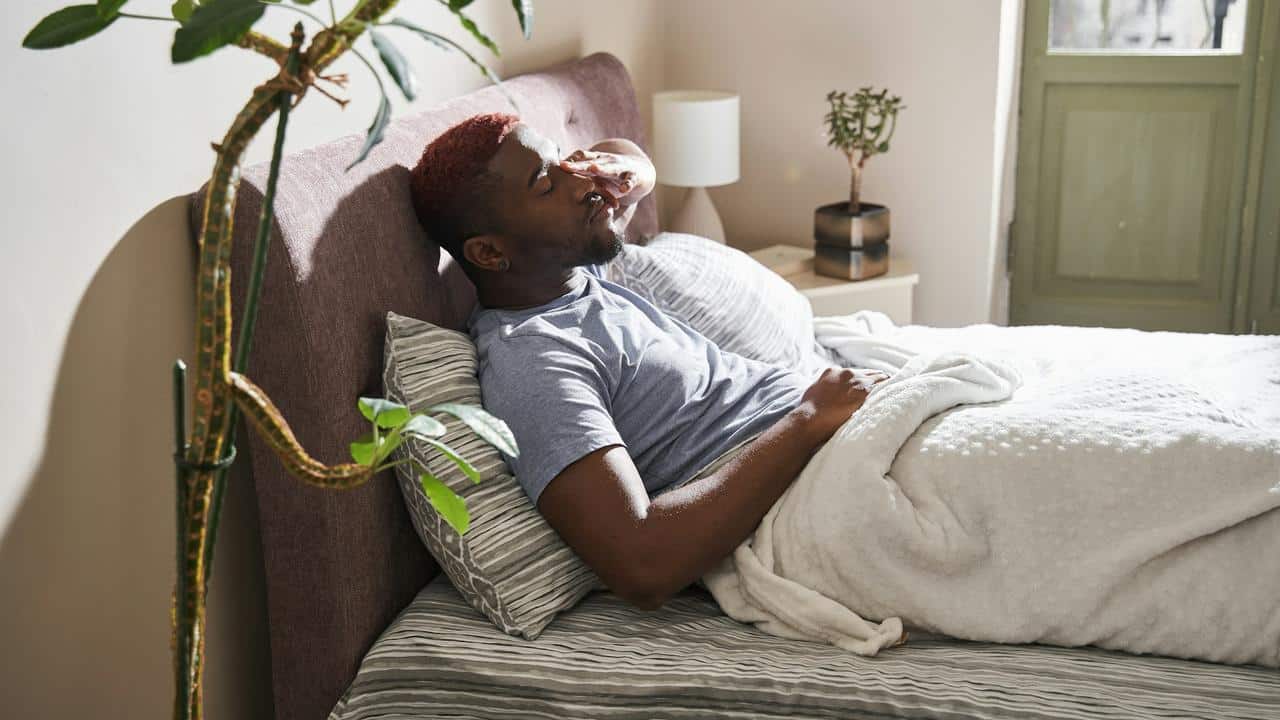 A man lying in bed covering his face.