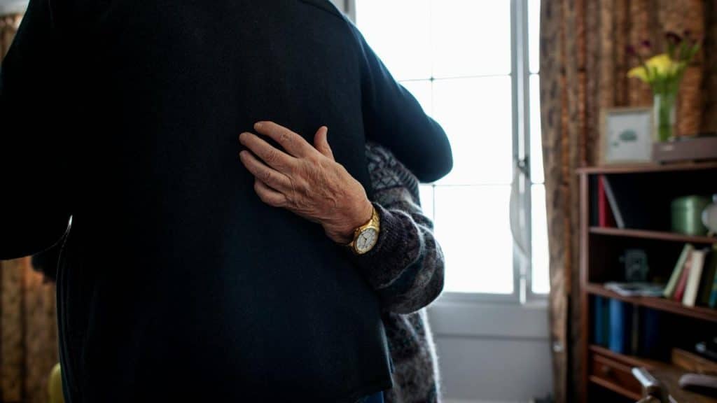 An older couple hugging in a warmly lit room.