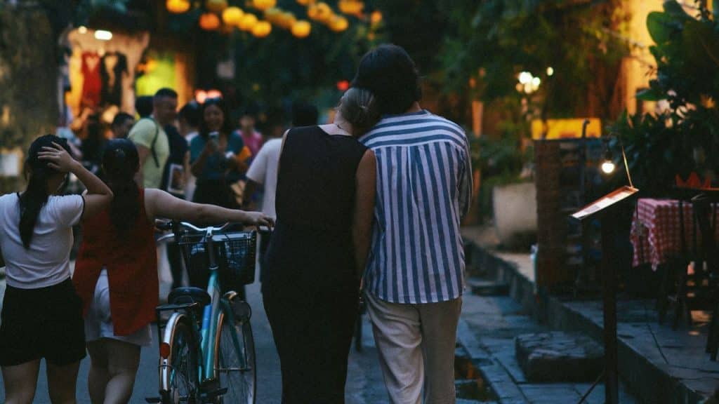 A view from behind of a couple walking down a dimly lit street at night.
