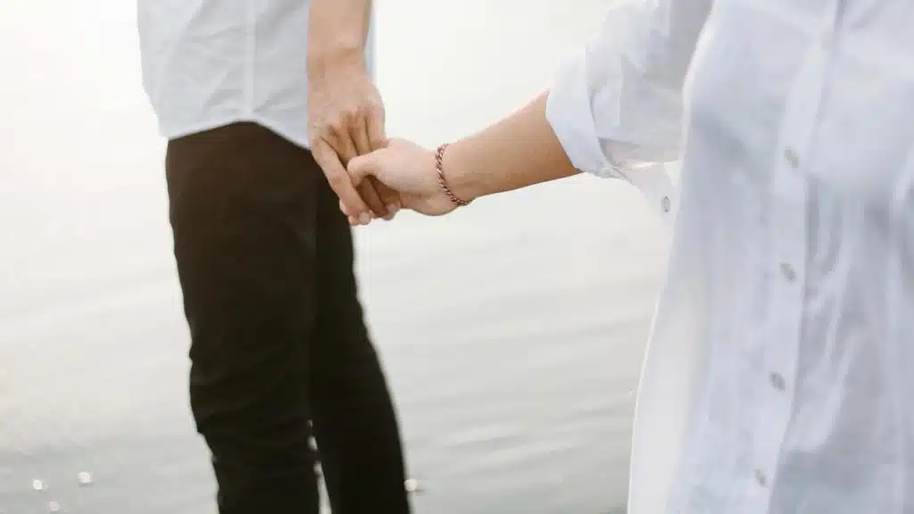 A man and woman holding hands while standing near water.