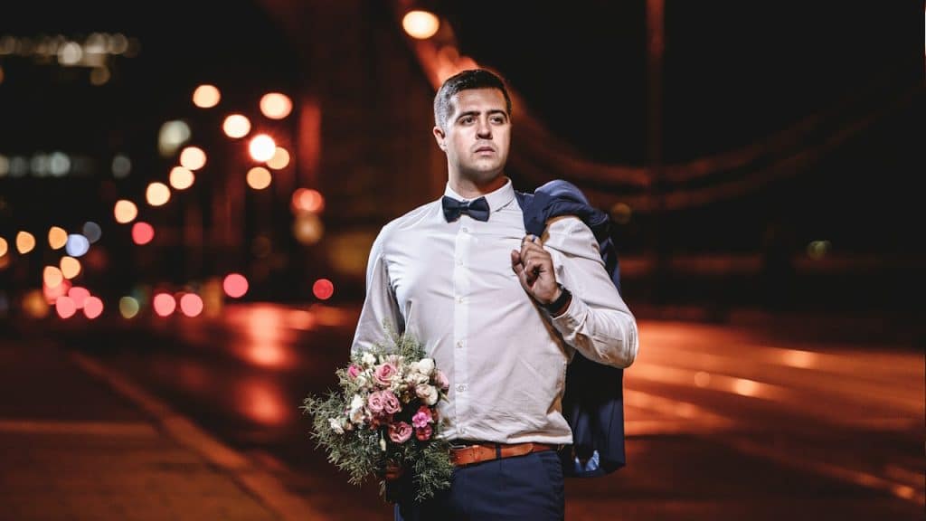 A man in a bow tie holding a bouquet of flowers.