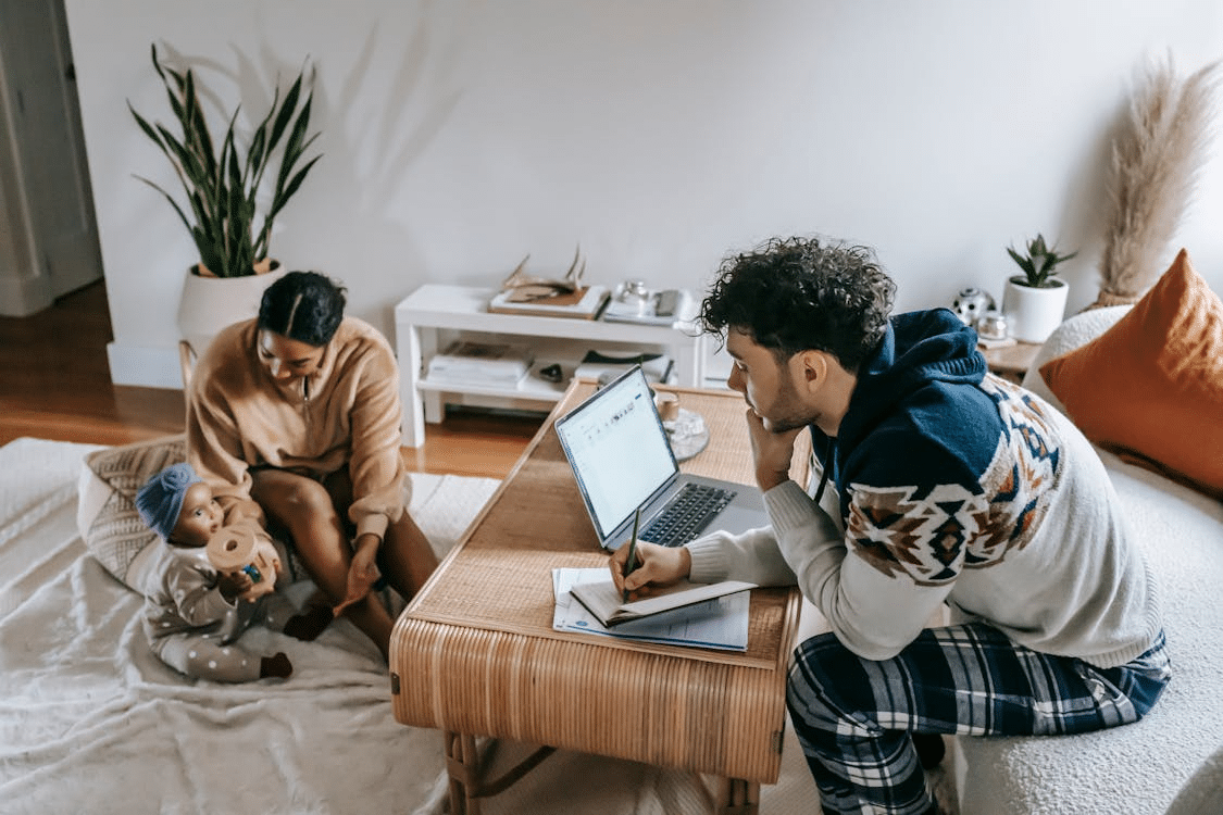 A man using a laptop and a woman sitting on the floor with a baby