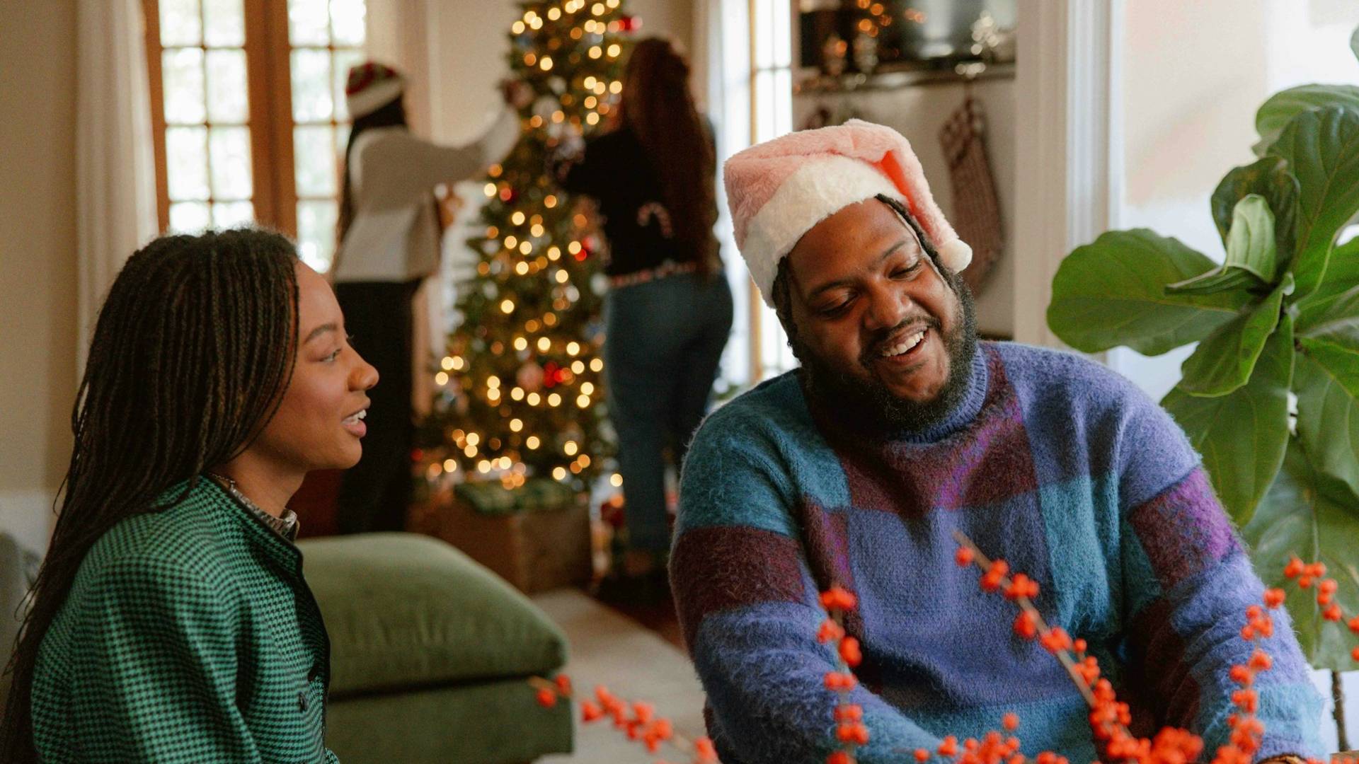 A couple talking while the two people are at the back, decorating a Christmas tree.