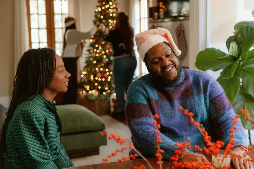 A couple talking while the two people are at the back, decorating a Christmas tree.